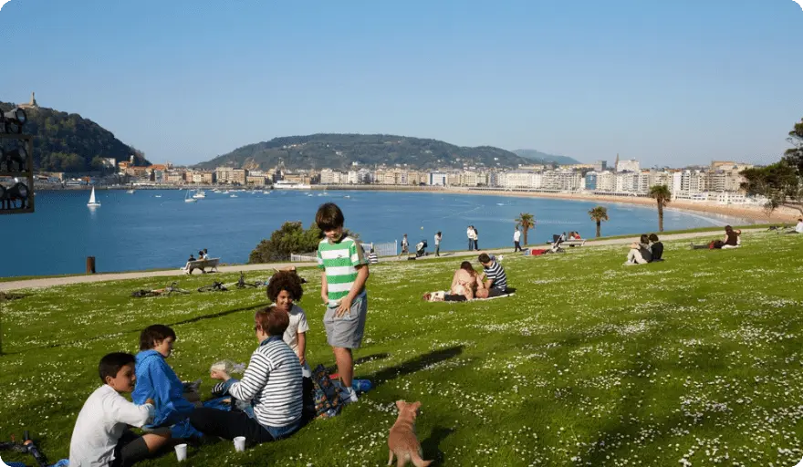 Personas sentadas en el césped del Palacio Miramar, con vistas a la bahía de la playa de La Concha.